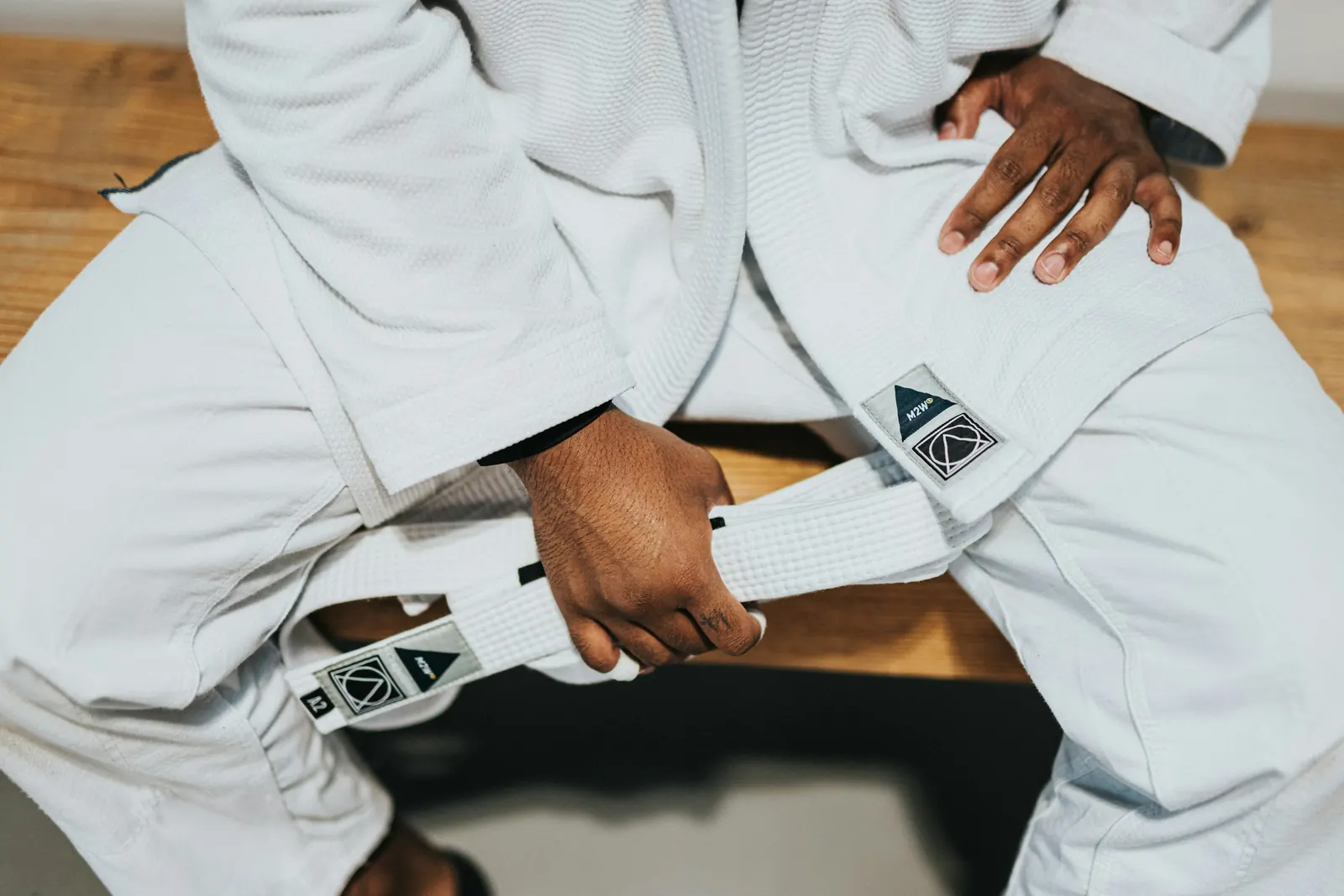 Gros plan sur un kimono blanc et une ceinture blanche tenue à la main, sur un banc en bois. Photo d’illustration.