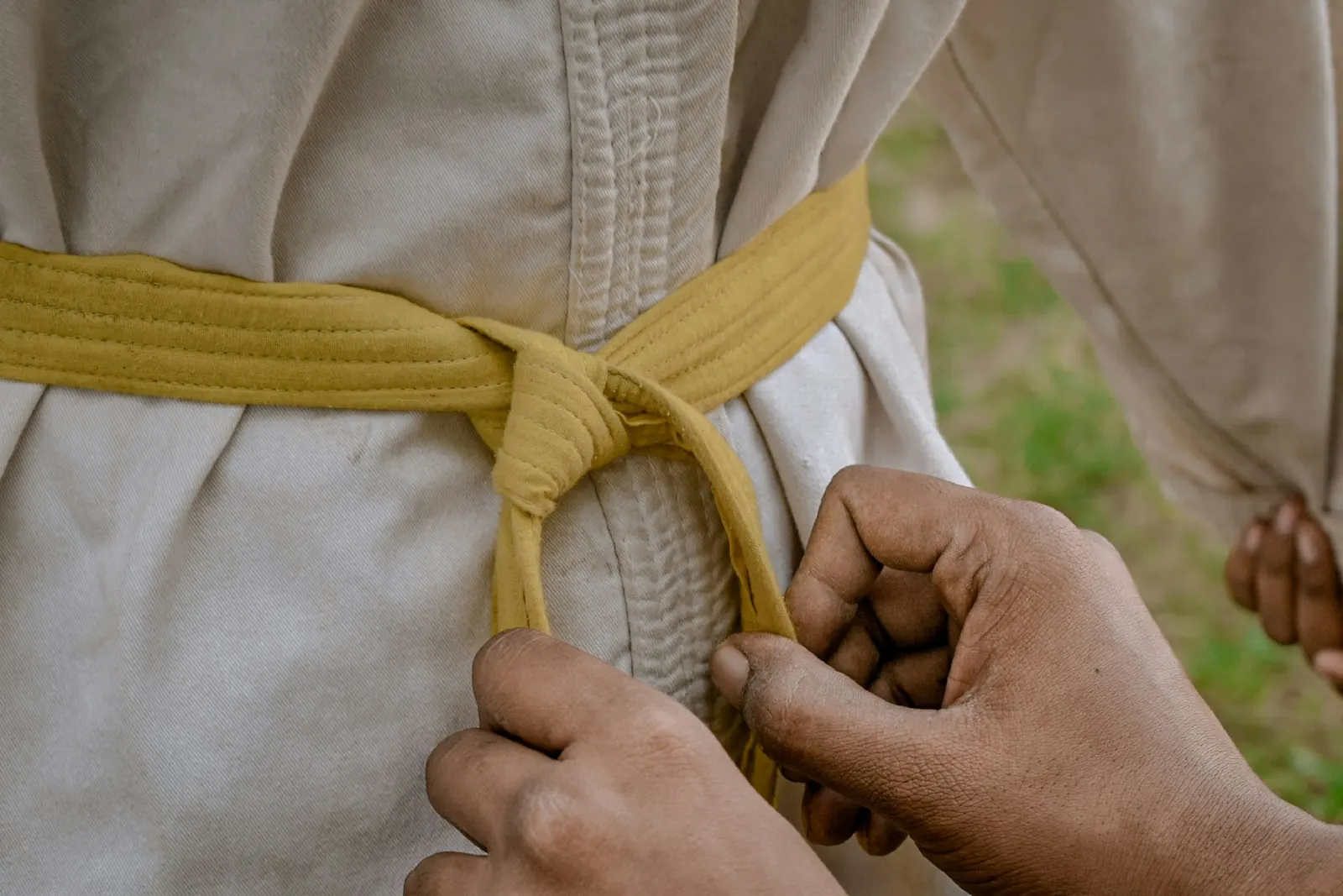 Deux mains nouent une ceinture jaune autour de la taille d’une personne en kimono clair. Photo d’illustration.