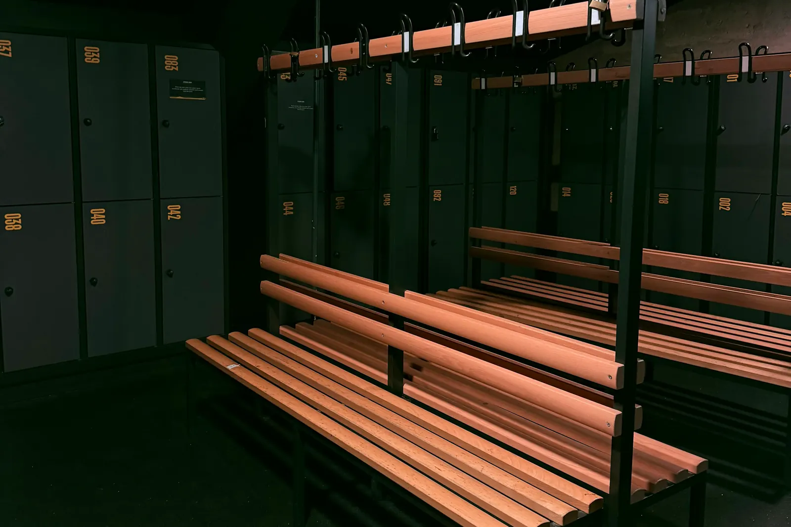 Un vestiaire vide et sombre, avec des bancs en bois et des casiers numérotés. Photo d’illustration.